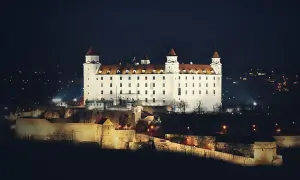 Biały zamek na wzgórzu nocą, z widokiem na miasto. To właśnie tutaj jest Bratysława, stolica Słowacji.