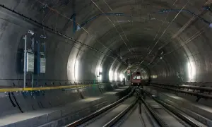 Pociąg wjeżdża do najdłuższego tunelu w Austrii. Betonowa konstrukcja, kable i oświetlenie tworzą mroczny, industrialny krajobraz.