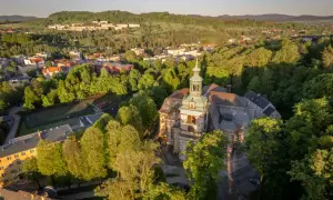 Widok z lotu ptaka na miasto otoczone zielenią, z dominującym kościołem i kamienna góra wrocław w tle.