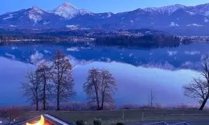 Spokojne jezioro odbija ośnieżone góry. W oddali lasy i miasteczko. Na pierwszym planie dach z księżycową lampą. Karyntia latem zachwyca.