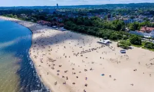 Plaża w Sopocie, do którego miast nad morzem można dojechać pociągiem z Warszawy. Tłumy ludzi odpoczywają na piasku.