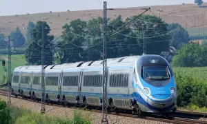 Szybki pociąg Pendolino mknie po torach, pokonując **drogę do Gdańska**. W tle zielone pola i drzewa.