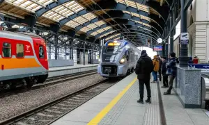 Lubuszanin pociąg na peronie, obok czerwono-pomarańczowy skład. Ludzie czekają na podróż.
