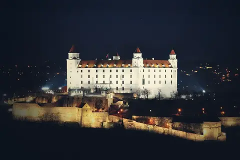 Biały zamek na wzgórzu nocą, z widokiem na miasto. To właśnie tutaj jest Bratysława, stolica Słowacji.