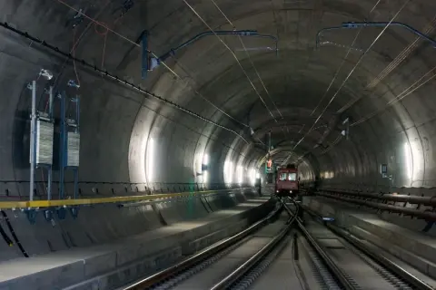 Pociąg wjeżdża do najdłuższego tunelu w Austrii. Betonowa konstrukcja, kable i oświetlenie tworzą mroczny, industrialny krajobraz.