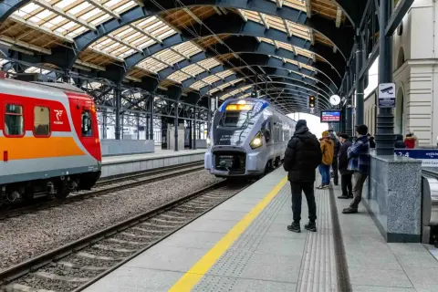 Lubuszanin pociąg na peronie, obok czerwono-pomarańczowy skład. Ludzie czekają na podróż.