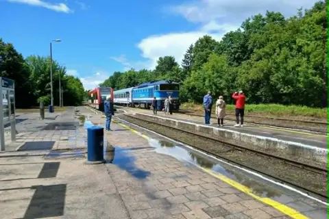 Na peronie czeka malczewski pociąg. Ludzie stoją na deszczu, czekając na podróż.
