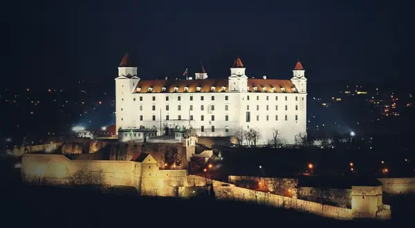 Biały zamek na wzgórzu nocą, z widokiem na miasto. To właśnie tutaj jest Bratysława, stolica Słowacji.