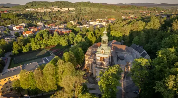 Widok z lotu ptaka na miasto otoczone zielenią, z dominującym kościołem i kamienna góra wrocław w tle.