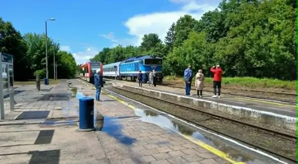 Na peronie czeka malczewski pociąg. Ludzie stoją na deszczu, czekając na podróż.