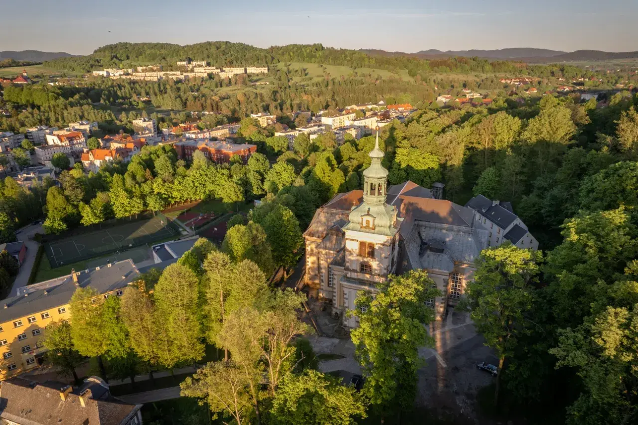 Widok z lotu ptaka na miasto otoczone zielenią, z dominującym kościołem i kamienna góra wrocław w tle.