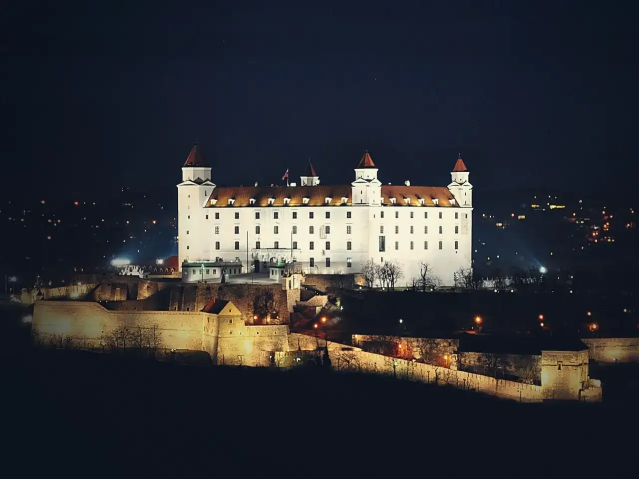 Biały zamek na wzgórzu nocą, z widokiem na miasto. To właśnie tutaj jest Bratysława, stolica Słowacji.