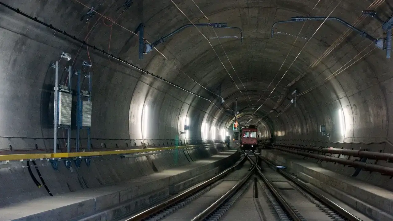 Pociąg wjeżdża do najdłuższego tunelu w Austrii. Betonowa konstrukcja, kable i oświetlenie tworzą mroczny, industrialny krajobraz.