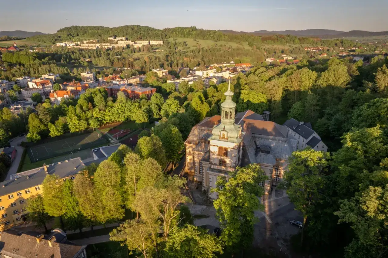 Widok z lotu ptaka na miasto otoczone zielenią, z dominującym kościołem i kamienna góra wrocław w tle.