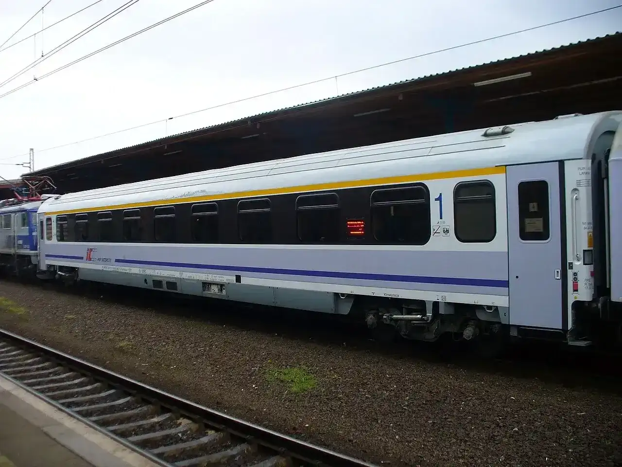 Biało-niebieski, komfortowy wagon kolejowy PKP Intercity z żółtym pasem, numerem "1" i klimatyzacją, gotowy do podróży.