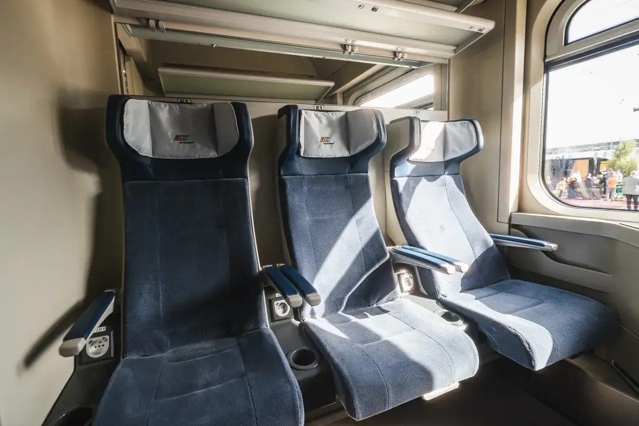 Komfortowy wagon kolejowy z trzema wygodnymi fotelami obok siebie. Jasne wnętrze, okno z widokiem na peron.
