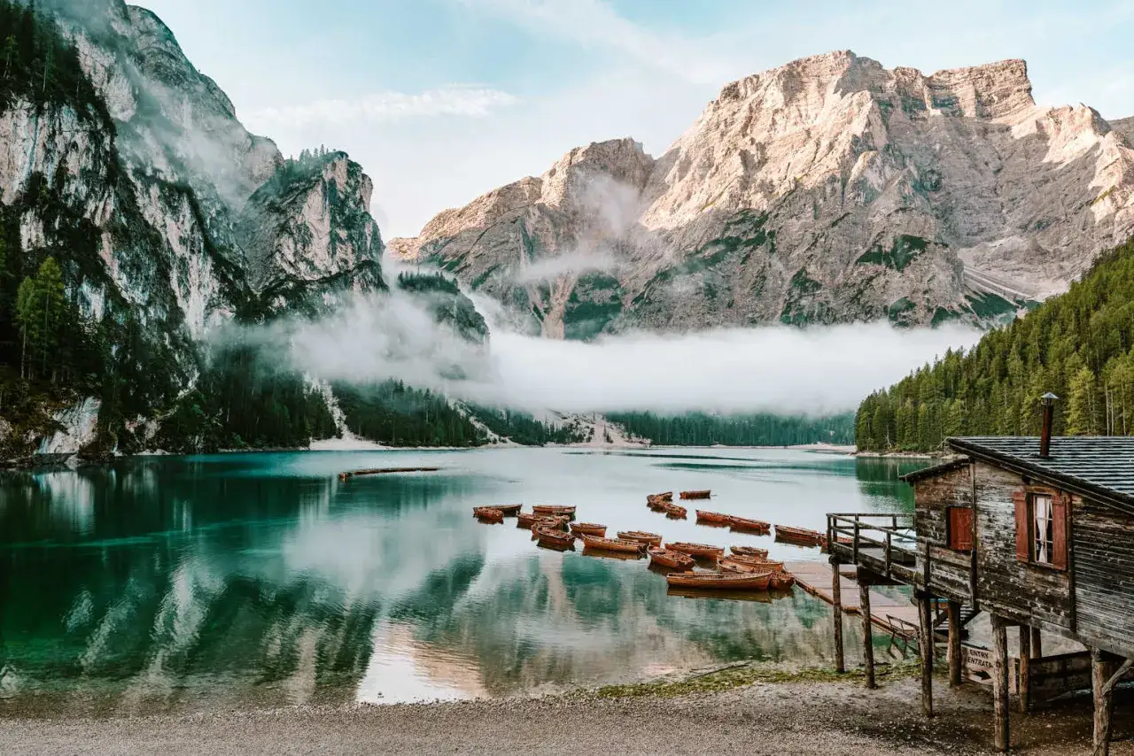 Gdzie jest Tyrol? Jezioro Braies w Dolomitach, otoczone mglistymi szczytami i lasami, z łodziami czekającymi na wodzie.