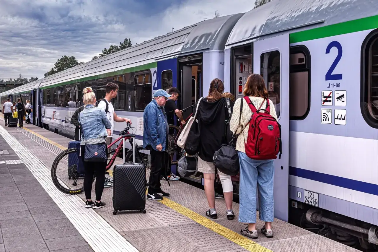Pasażerowie z bagażami i rowerami czekają na pociąg. Wszyscy odczuwają ulga ustawowa, bo podróż wreszcie się rozpoczyna.