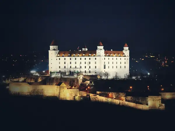 Biały zamek na wzgórzu nocą, z widokiem na miasto. To właśnie tutaj jest Bratysława, stolica Słowacji.