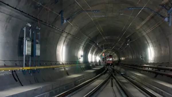 Pociąg wjeżdża do najdłuższego tunelu w Austrii. Betonowa konstrukcja, kable i oświetlenie tworzą mroczny, industrialny krajobraz.