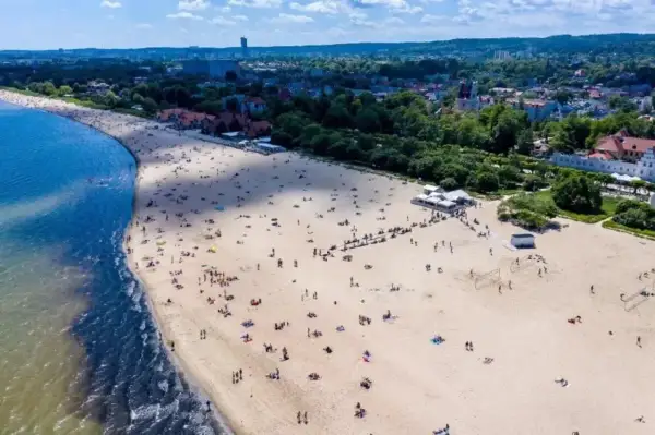 Plaża w Sopocie, do którego miast nad morzem można dojechać pociągiem z Warszawy. Tłumy ludzi odpoczywają na piasku.