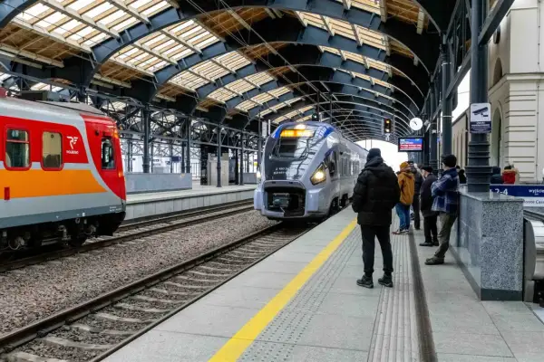 Lubuszanin pociąg na peronie, obok czerwono-pomarańczowy skład. Ludzie czekają na podróż.
